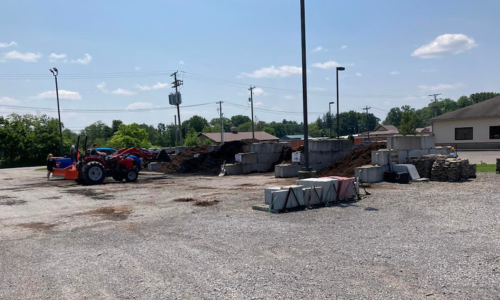 A tractor driving toward piles of mulch & soil in an open area with a clear sky