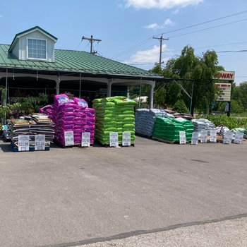 Several bags of potting soil and mulch stacked outside the front of a store.